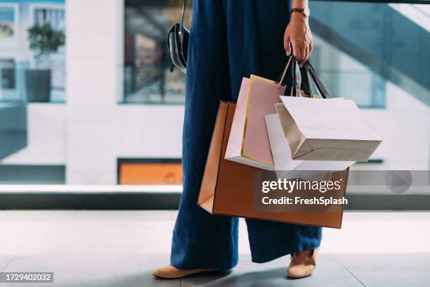 An unrecognizable Caucasian female standing at the shopping mall with paper bags.